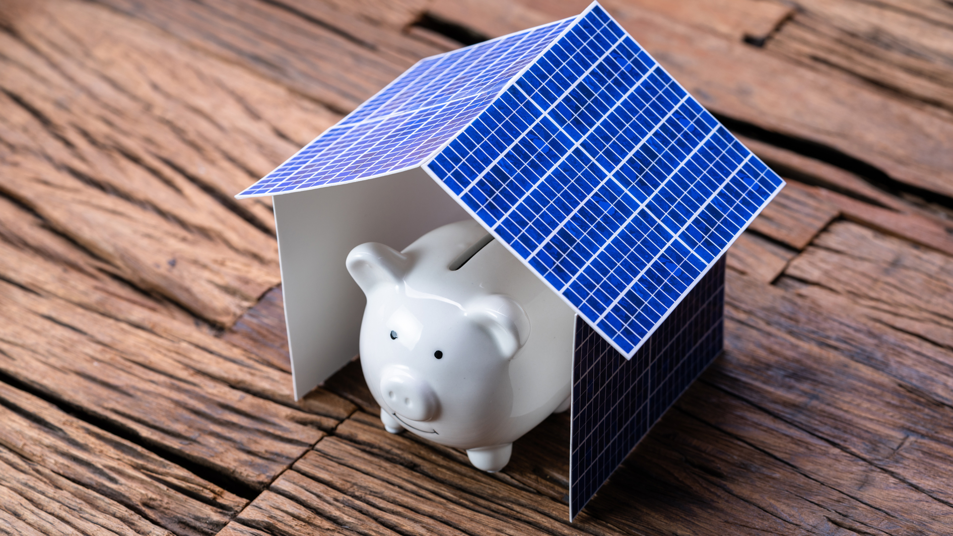 Salvadanaio a forma di maialino sotto tetto di pannelli fotovoltaici, simbolo di risparmio e agevolazioni fiscali